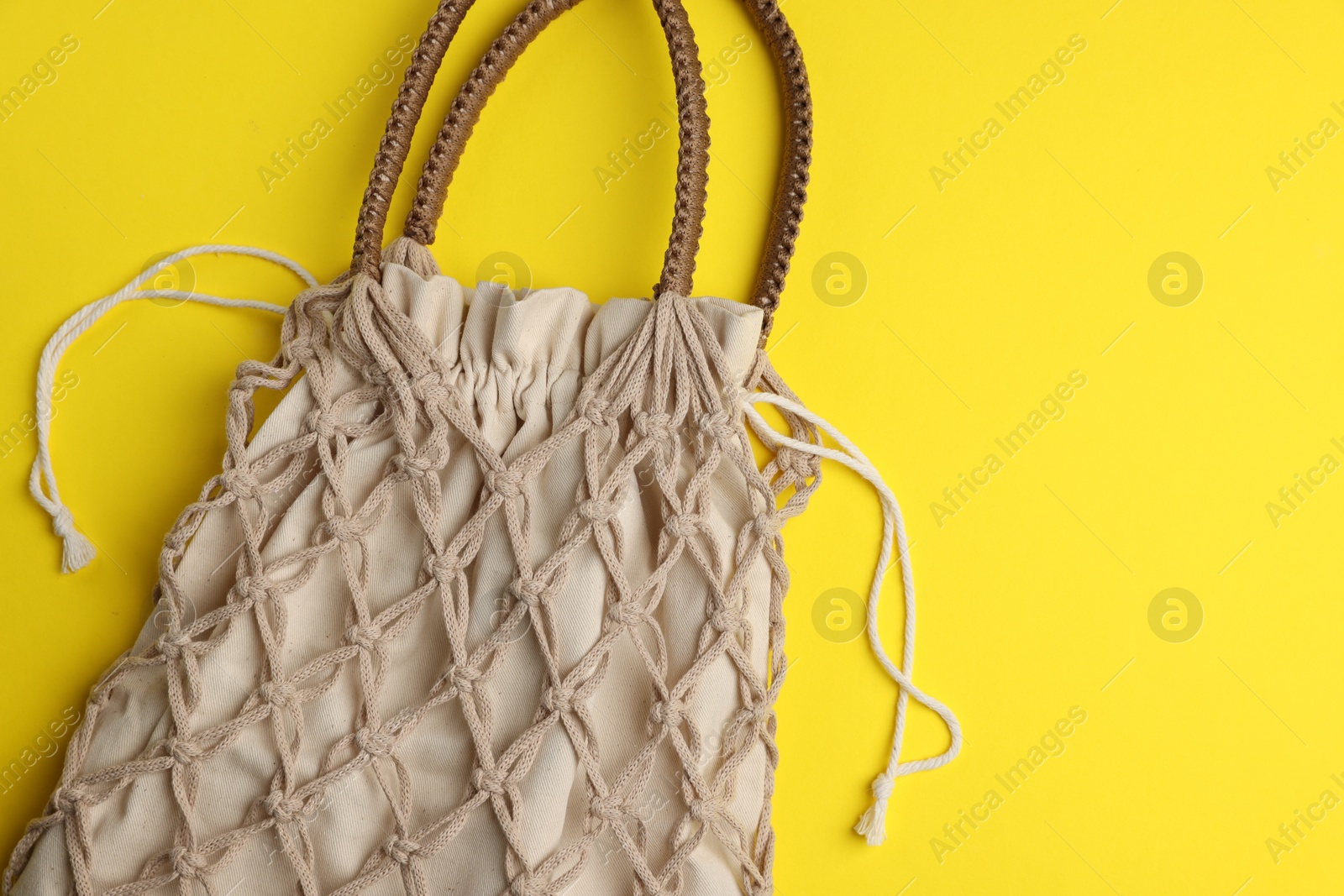 Photo of Macrame shopping bag on yellow background, top view. Space for text