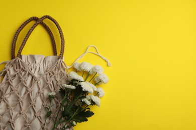 Photo of Macrame shopping bag and flowers on yellow background, top view. Space for text