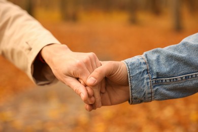 Photo of Couple holding hands in autumn park, closeup