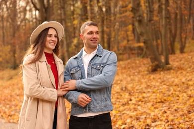 Photo of Happy couple spending time together in autumn park, space for text