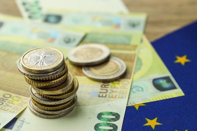 Photo of Euro banknotes, coins and European Union flag on table, closeup