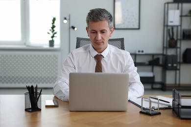 Photo of Middle aged man working with laptop at table in office