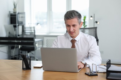 Photo of Middle aged man working with laptop at table in office