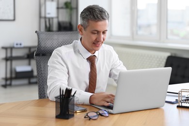 Photo of Middle aged man working with laptop at table in office