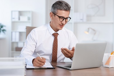 Photo of Middle aged man having videochat by laptop at table in office