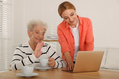 Photo of Caregiver showing something on laptop to senior woman at home