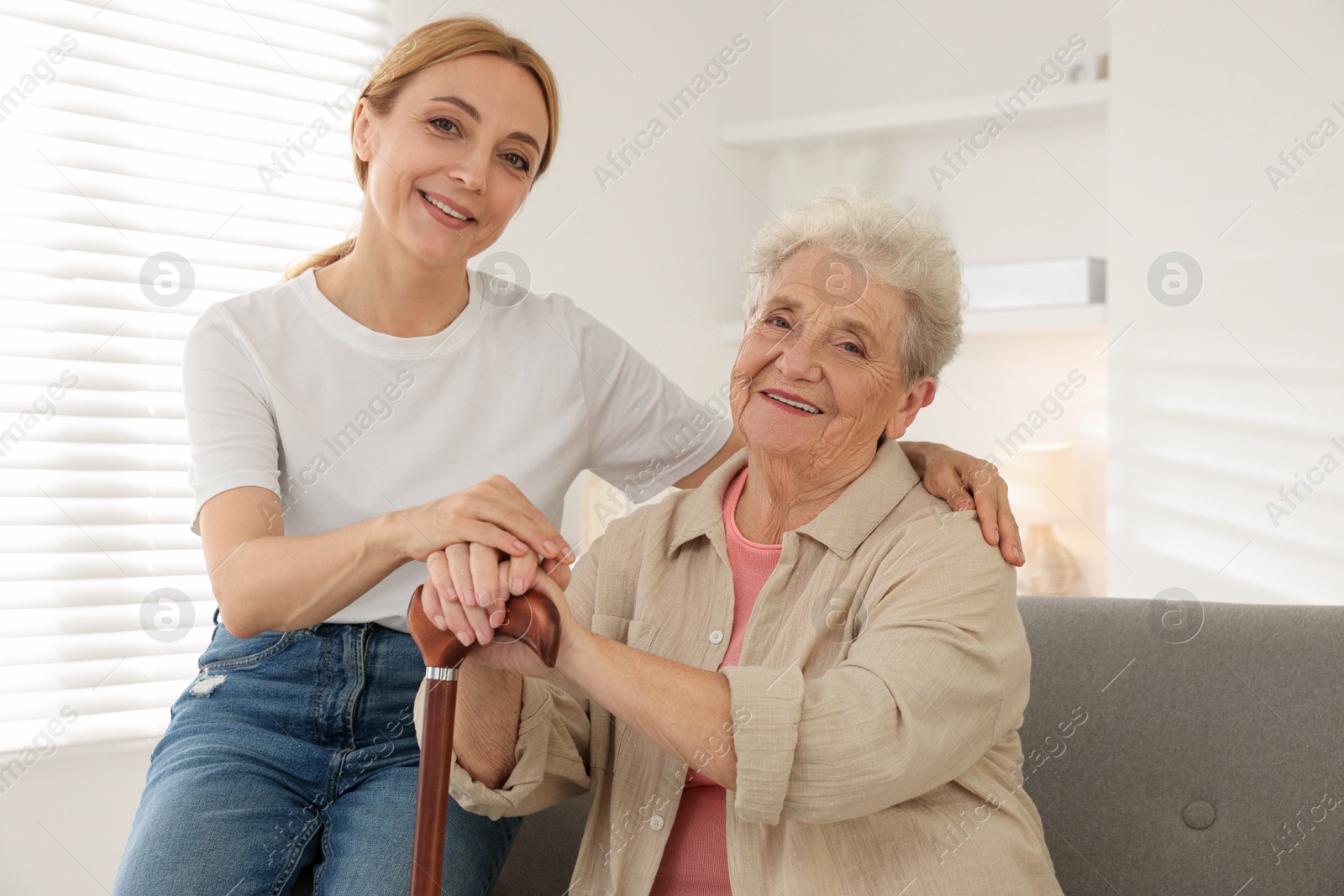 Photo of Caregiver supporting senior woman in living room at home