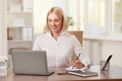 Smiling middle aged woman working with laptop at table in office