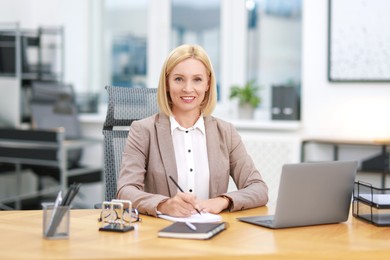 Photo of Portrait of smiling middle aged woman at table in office