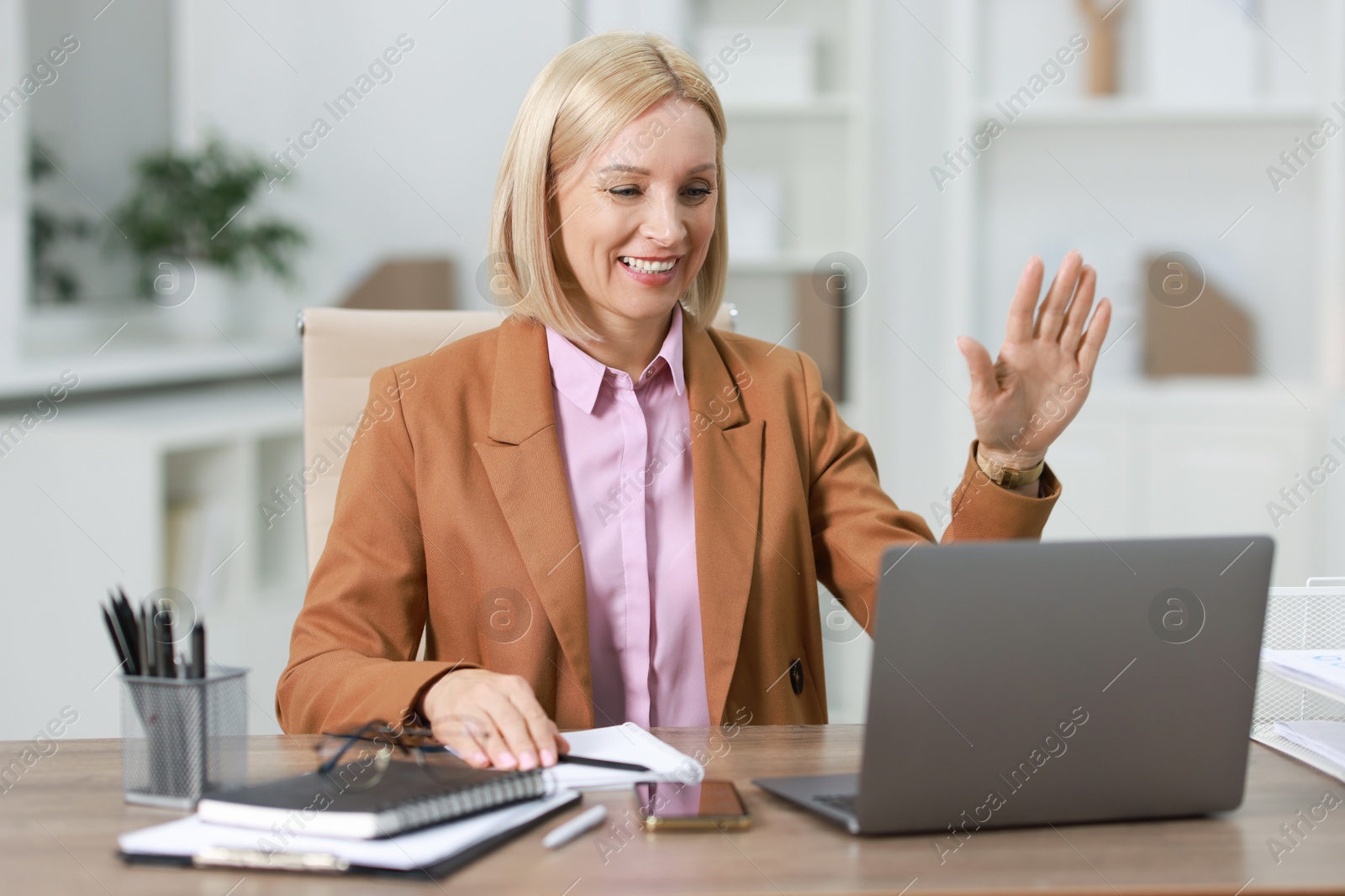 Photo of Smiling middle aged woman having videochat by laptop at table in office