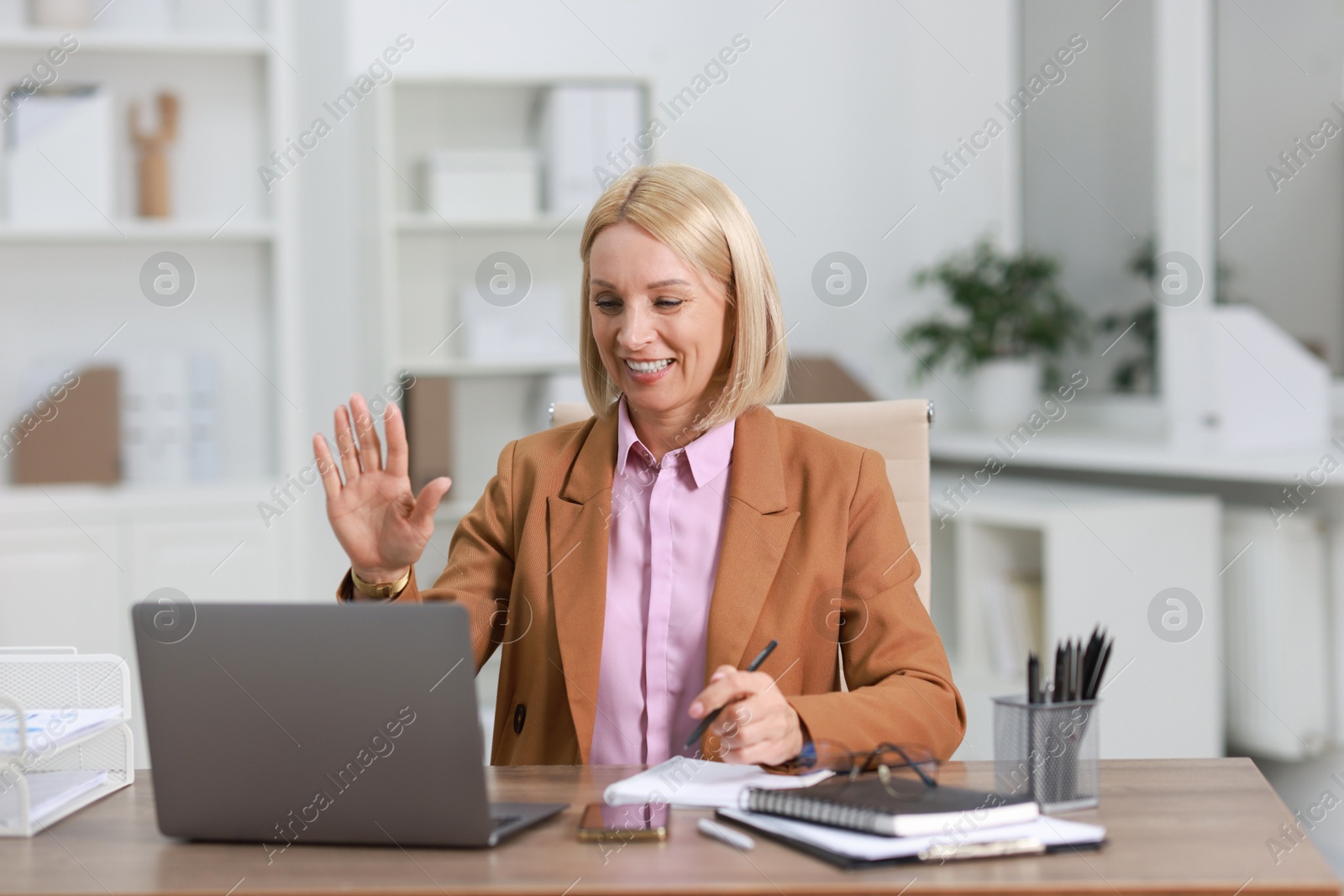 Photo of Smiling middle aged woman having videochat by laptop at table in office