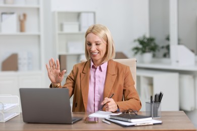 Photo of Smiling middle aged woman having videochat by laptop at table in office