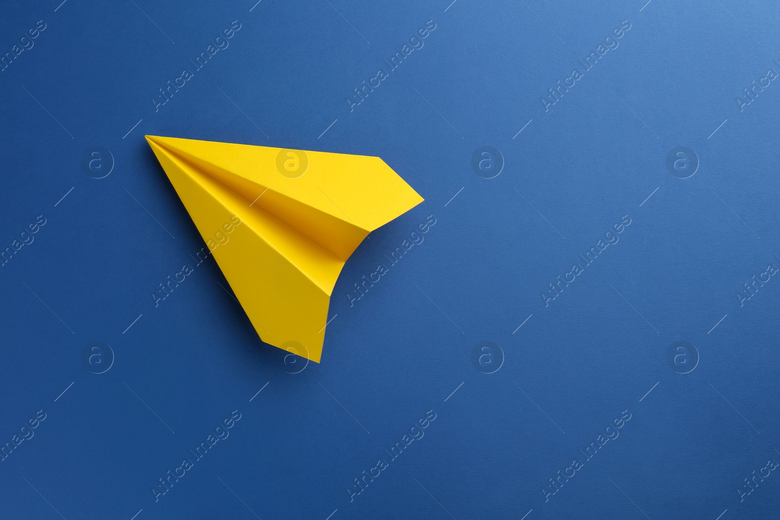 Photo of One handmade yellow paper plane on blue background, top view. Space for text