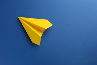 Photo of One handmade yellow paper plane on blue background, top view. Space for text