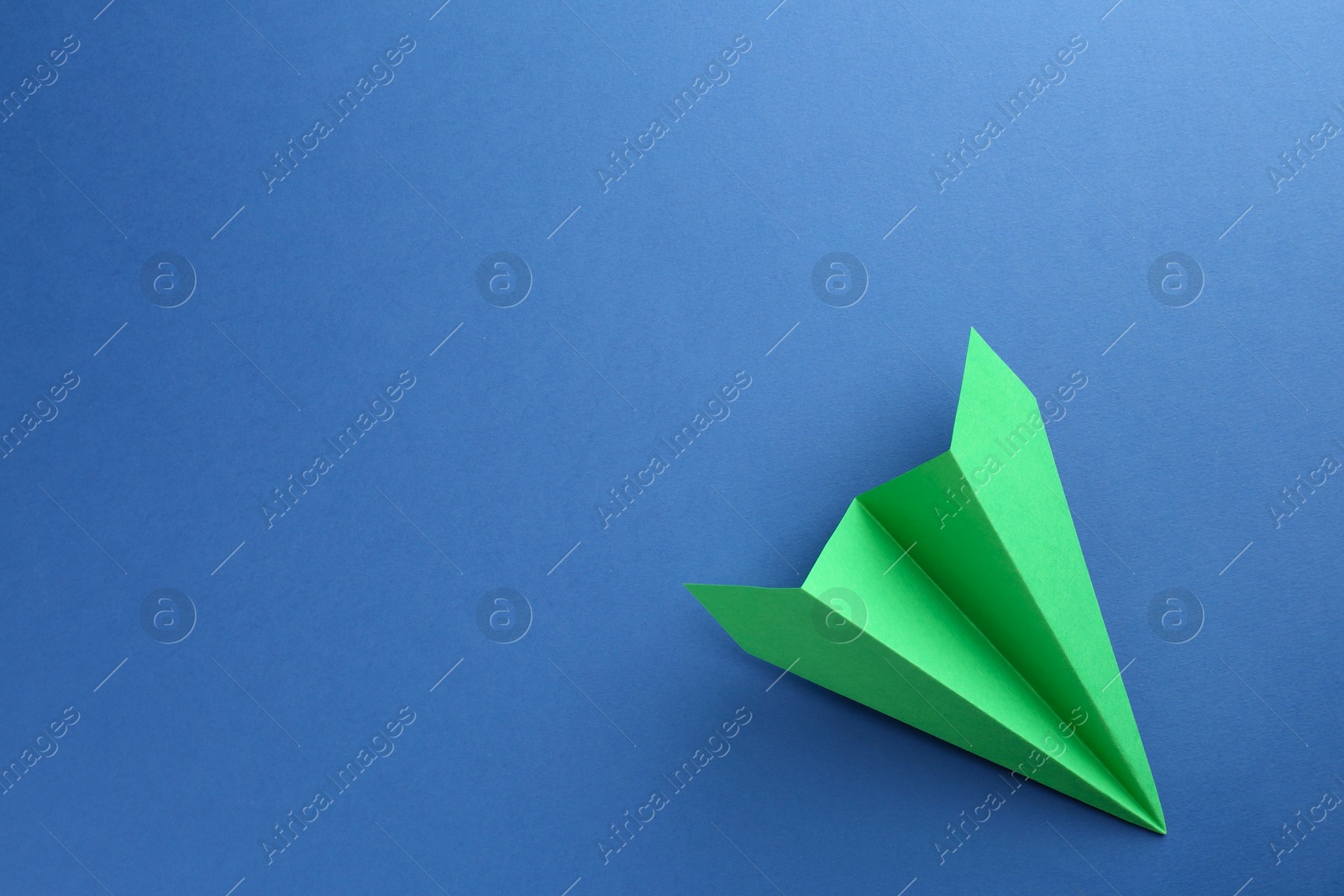 Photo of One handmade green paper plane on blue background, top view. Space for text