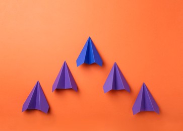 Photo of Handmade color paper planes on orange background, flat lay