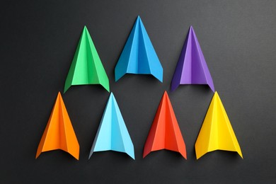 Colorful paper planes on black background, top view