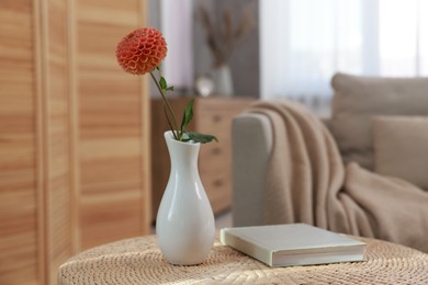 Book and vase with beautiful dahlia flower on wicker side table in living room