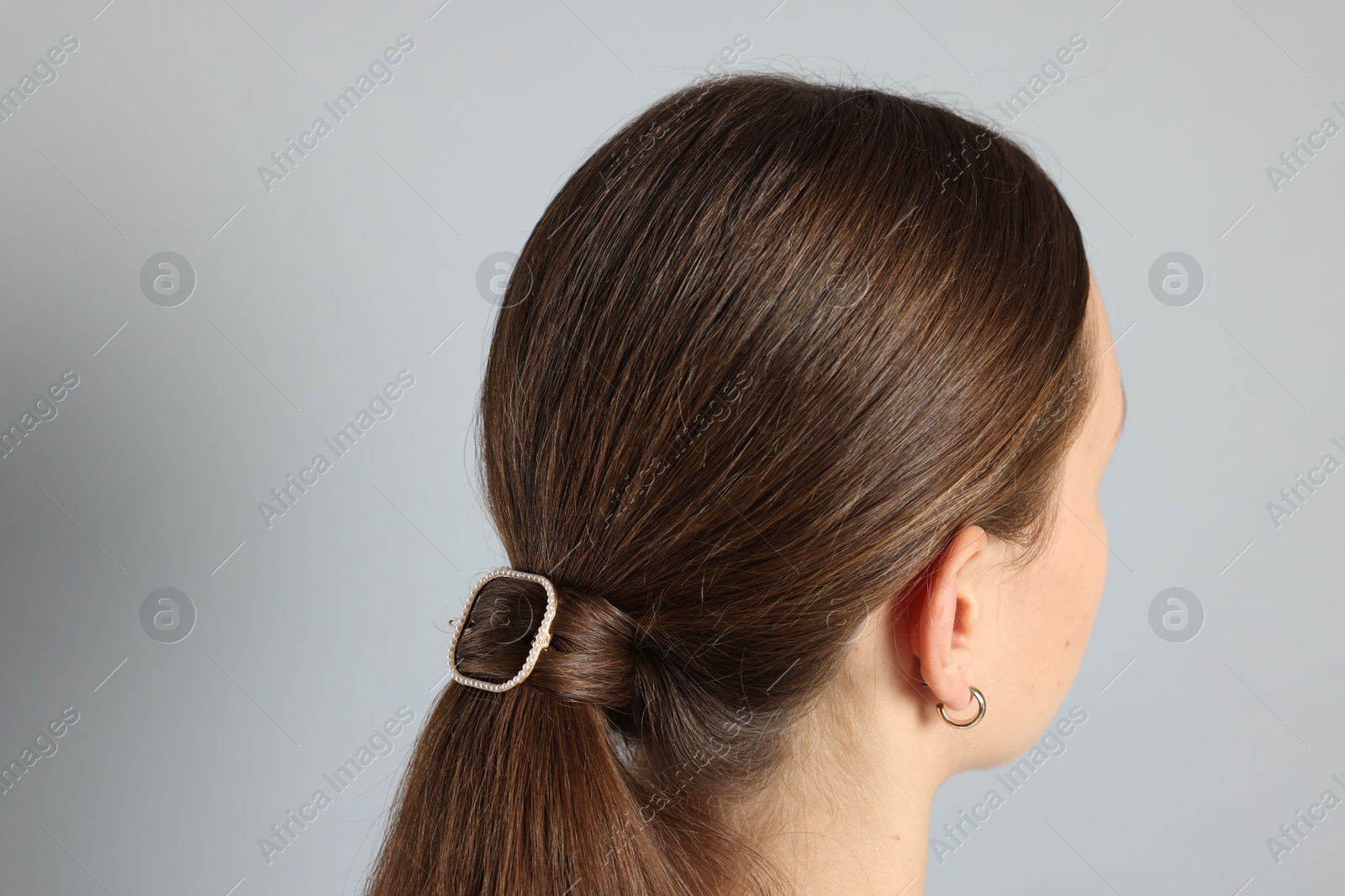 Photo of Teenage girl with stylish hair clip on light grey background, back view