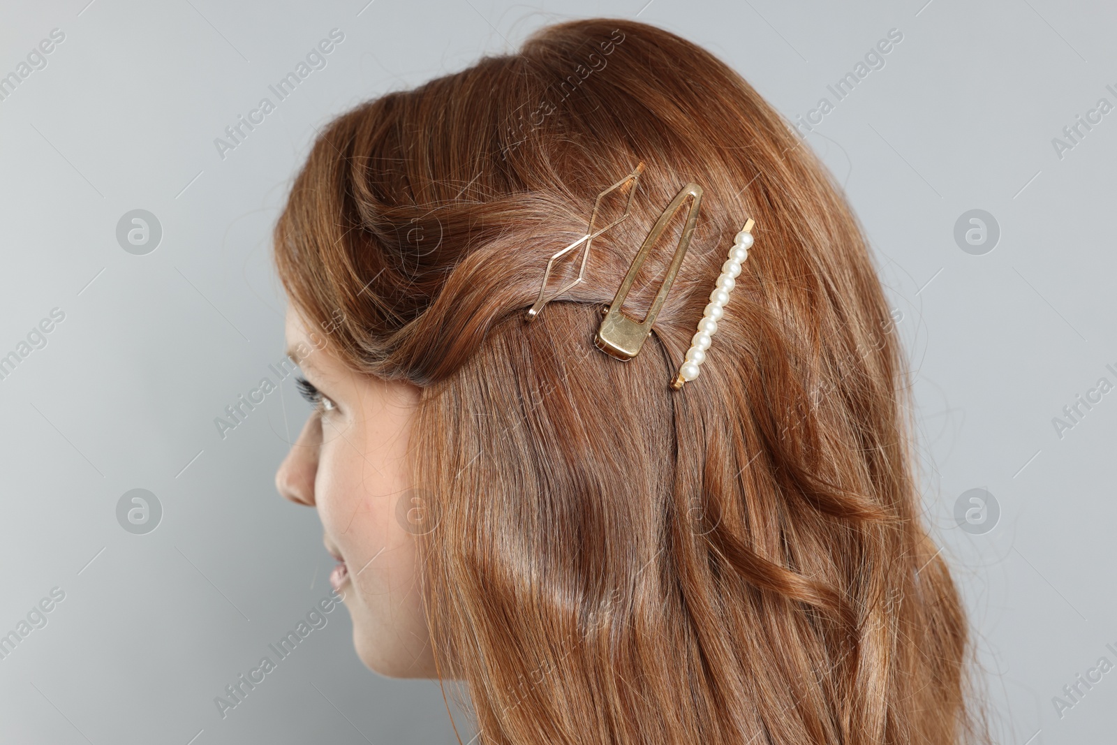 Photo of Teenage girl with stylish hair clips on light grey background, closeup