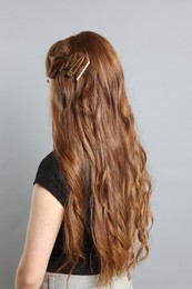 Photo of Teenage girl with stylish hair clips on light grey background, back view