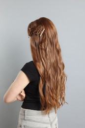 Photo of Teenage girl with stylish hair clips on light grey background, back view