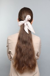 Photo of Teenage girl with stylish hair band on light grey background, back view