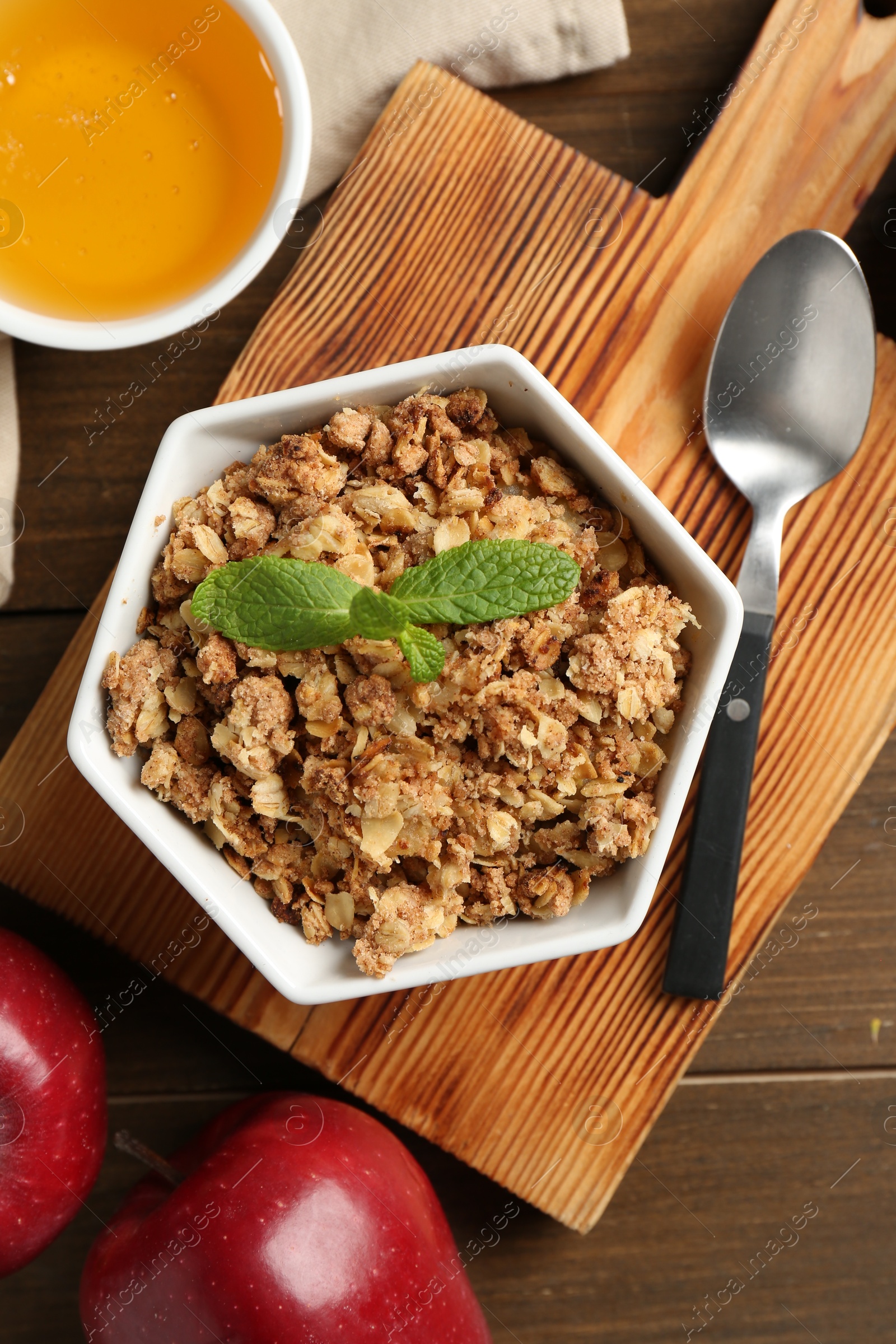 Photo of Tasty apple crisp in bowl, fresh fruits, honey and spoon on wooden table, flat lay