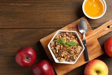 Photo of Tasty apple crisp in bowl, fresh fruits, honey and spoon on wooden table, flat lay. Space for text