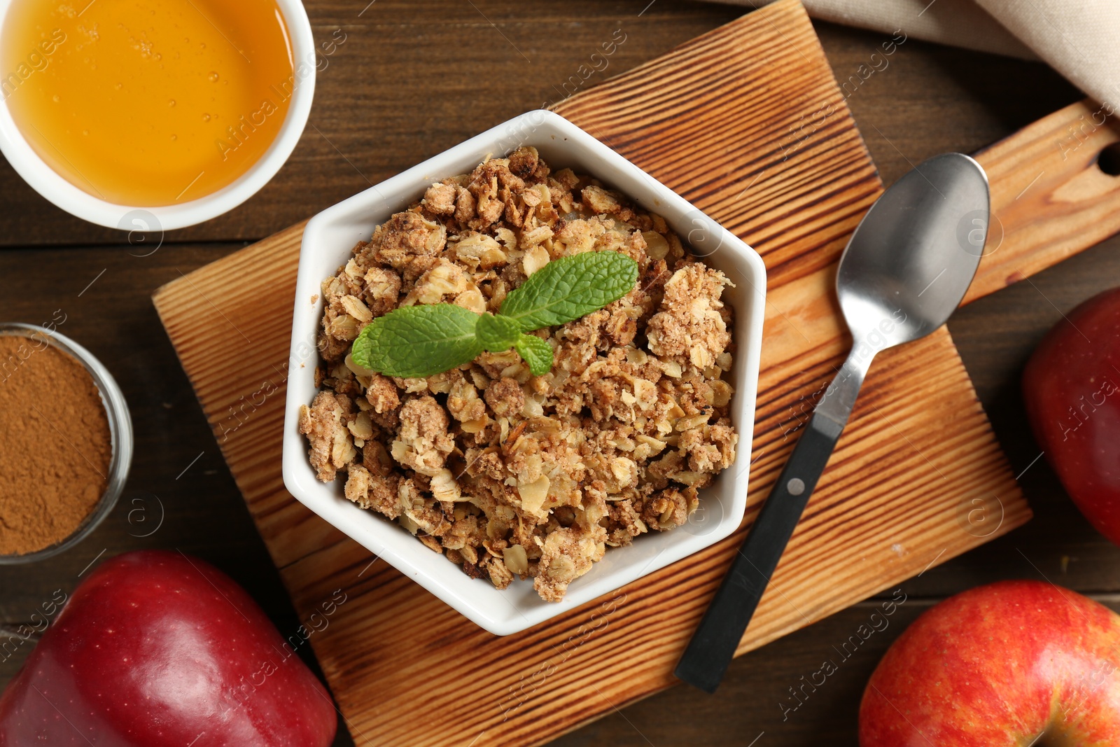 Photo of Tasty apple crisp in bowl, ingredients and spoon on wooden table, flat lay