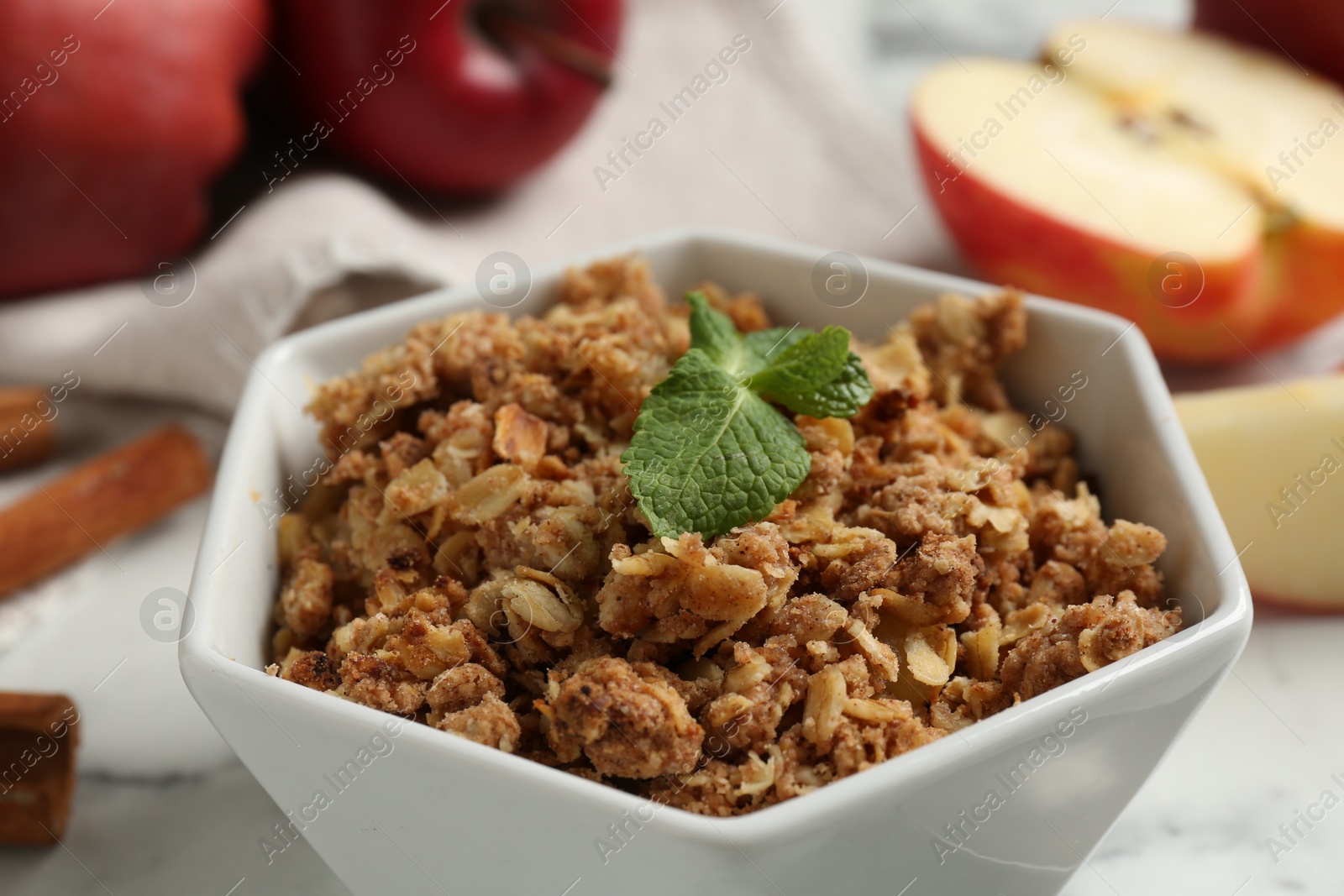 Photo of Tasty apple crisp in bowl and fresh fruits on light table, closeup