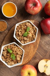 Tasty apple crisp in bowls and ingredients on wooden table, flat lay