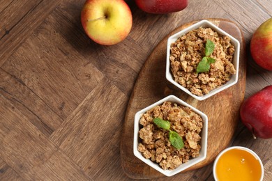 Photo of Tasty apple crisp in bowls, fresh fruits and honey on wooden table, flat lay. Space for text