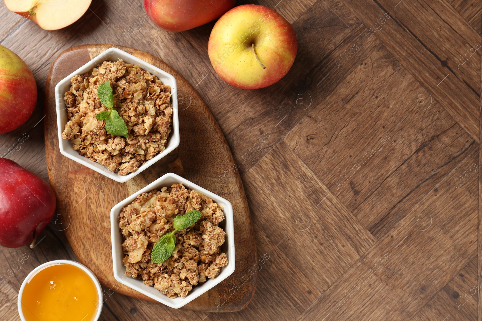 Photo of Tasty apple crisp in bowls, fresh fruits and honey on wooden table, flat lay. Space for text