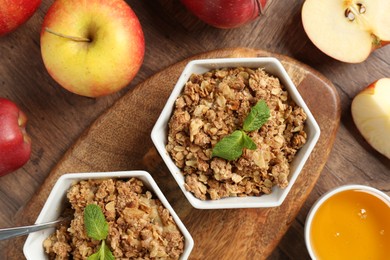 Photo of Tasty apple crisp in bowls, fresh fruits and honey on wooden table, flat lay