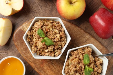 Photo of Tasty apple crisp in bowls, fresh fruits and honey on wooden table, flat lay