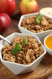 Tasty apple crisp in bowls, fresh fruits, honey and spoon on table, closeup