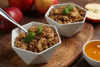 Tasty apple crisp in bowls, fresh fruits, honey and spoon on wooden table, closeup