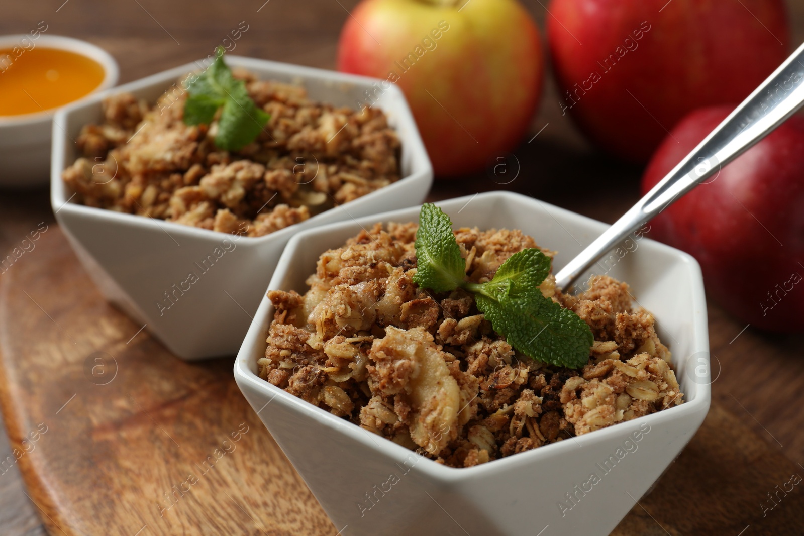 Photo of Tasty apple crisp in bowls, fresh fruits and spoon on table, closeup