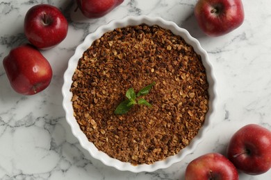 Photo of Tasty apple crisp in baking dish and fresh fruits on white marble table, flat lay