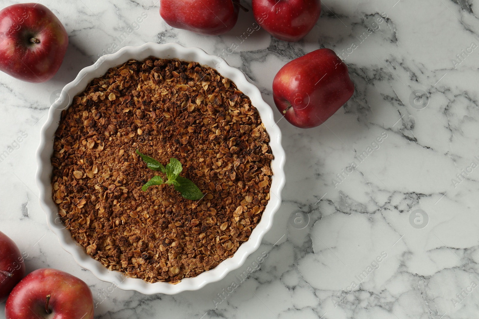 Photo of Tasty apple crisp in baking dish and fresh fruits on white marble table, flat lay. Space for text