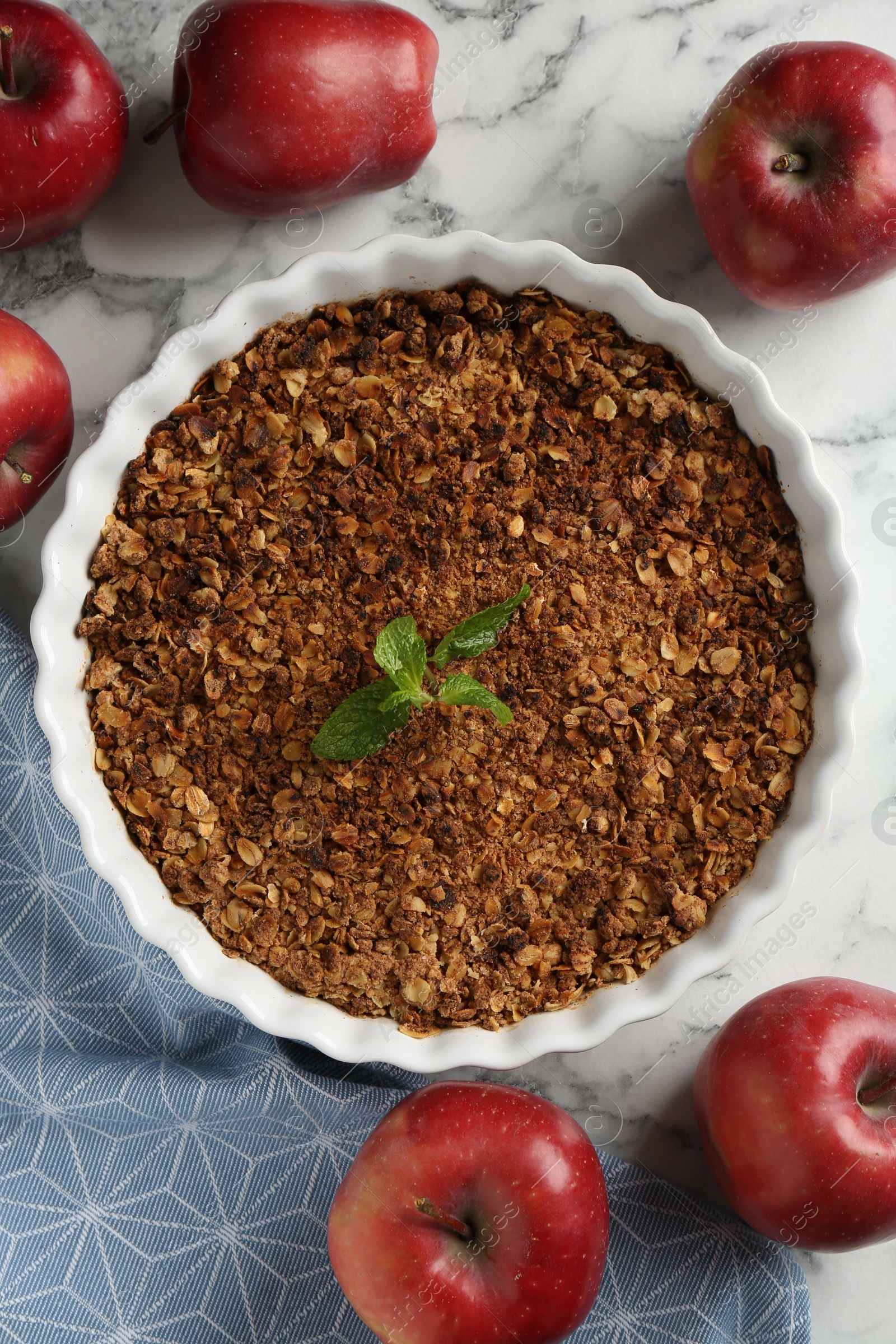 Photo of Tasty apple crisp in baking dish and fresh fruits on white marble table, flat lay