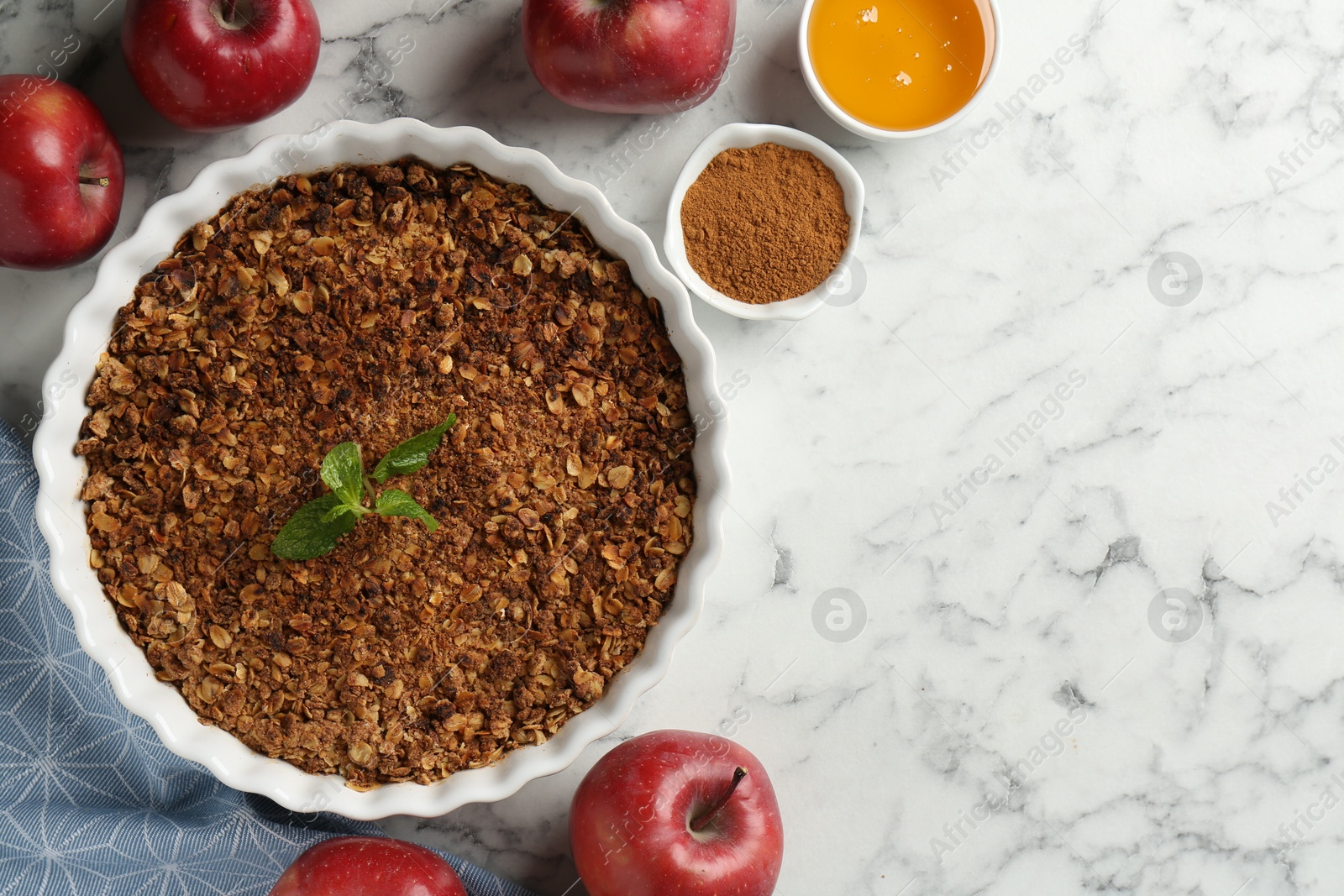 Photo of Tasty apple crisp in baking dish and ingredients on white marble table, flat lay. Space for text