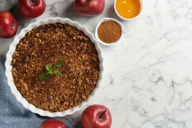 Photo of Tasty apple crisp in baking dish and ingredients on white marble table, flat lay. Space for text