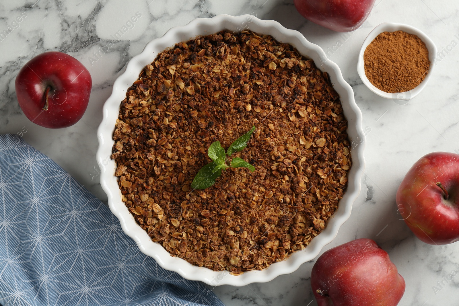 Photo of Tasty apple crisp in baking dish, fresh fruits and cinnamon on white marble table, flat lay