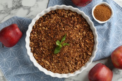 Photo of Tasty apple crisp in baking dish, fresh fruits and cinnamon on white marble table, flat lay