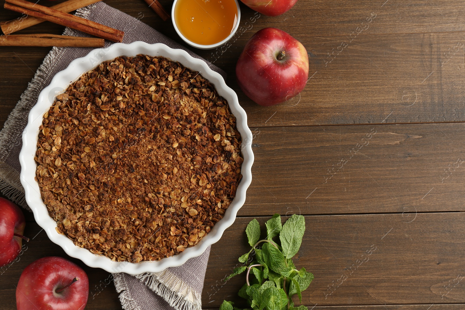 Photo of Tasty apple crisp in baking dish and ingredients on wooden table, flat lay. Space for text