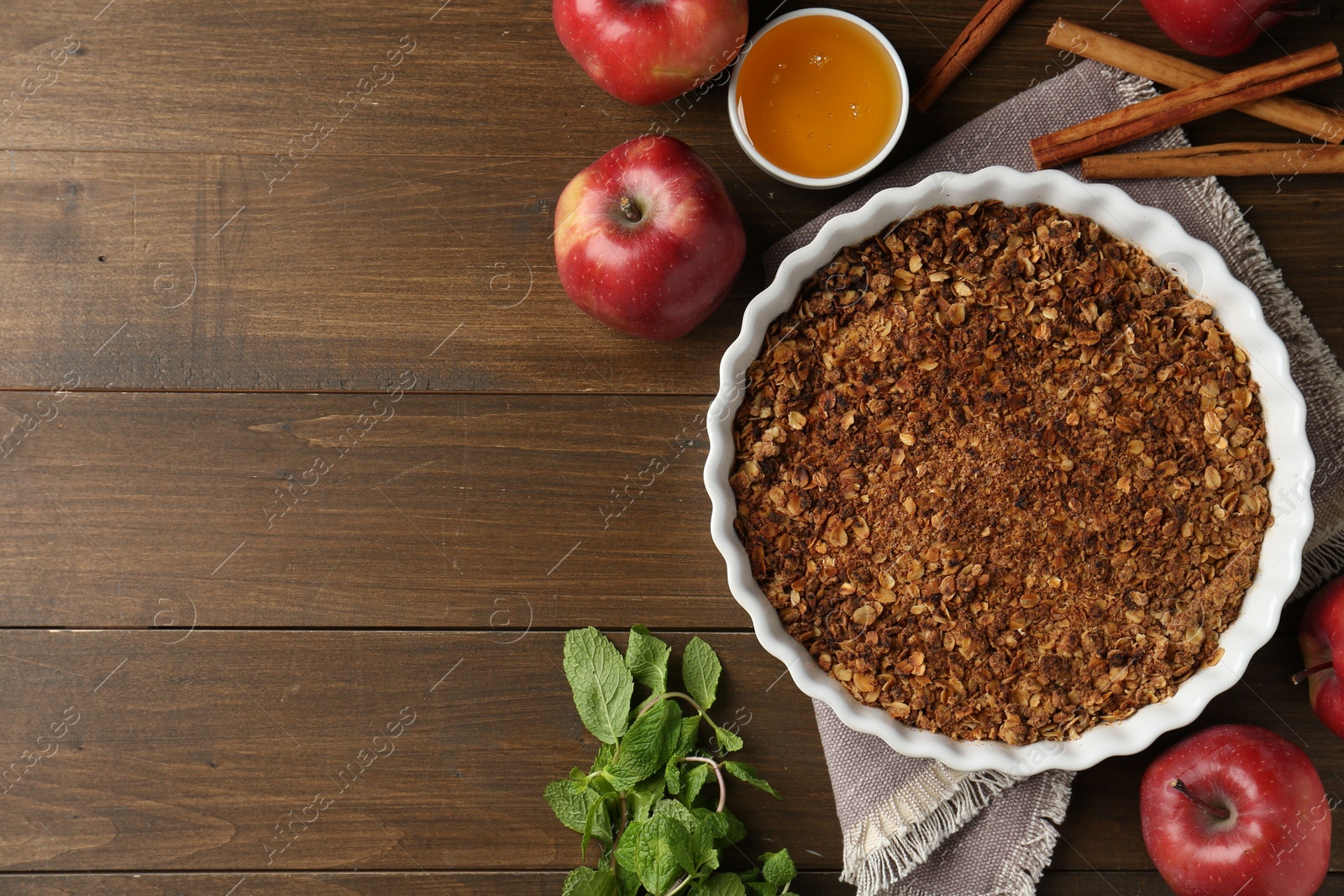 Photo of Tasty apple crisp in baking dish and ingredients on wooden table, flat lay. Space for text