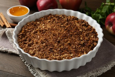 Tasty apple crisp in baking dish and ingredients on wooden table, closeup