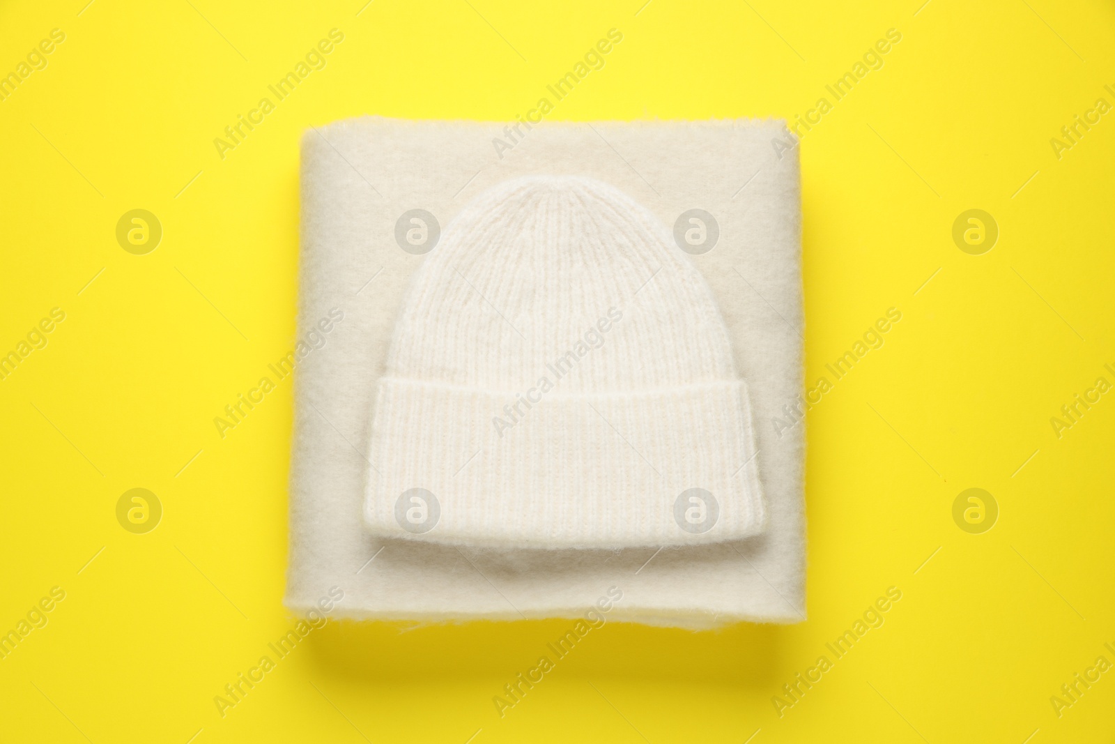 Photo of Warm woolen hat and scarf on yellow background, top view